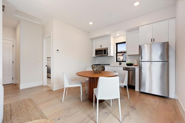 kitchen with light countertops, decorative backsplash, appliances with stainless steel finishes, white cabinets, and light wood-type flooring