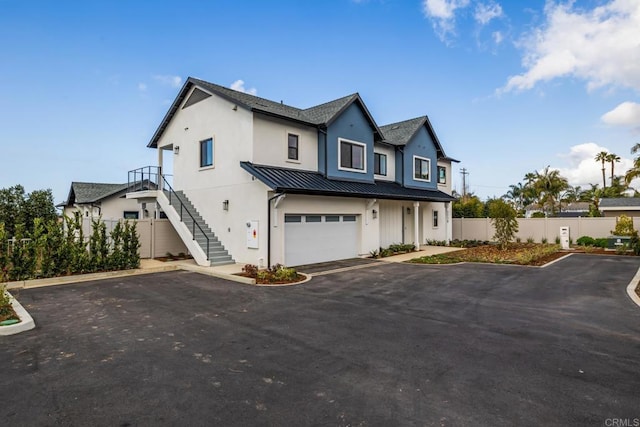 modern farmhouse style home featuring stairway, aphalt driveway, metal roof, a standing seam roof, and fence