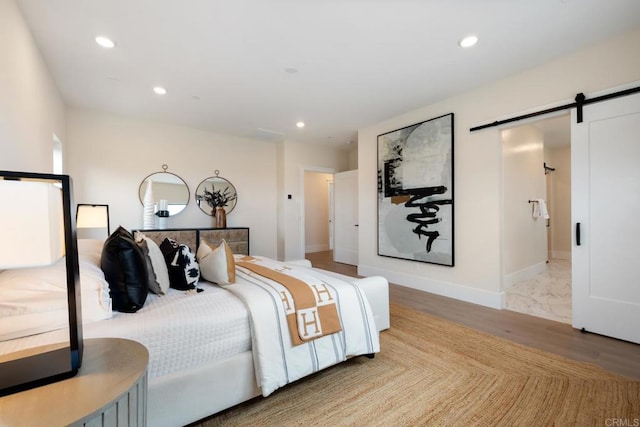 bedroom featuring baseboards, a barn door, light wood-style floors, and recessed lighting