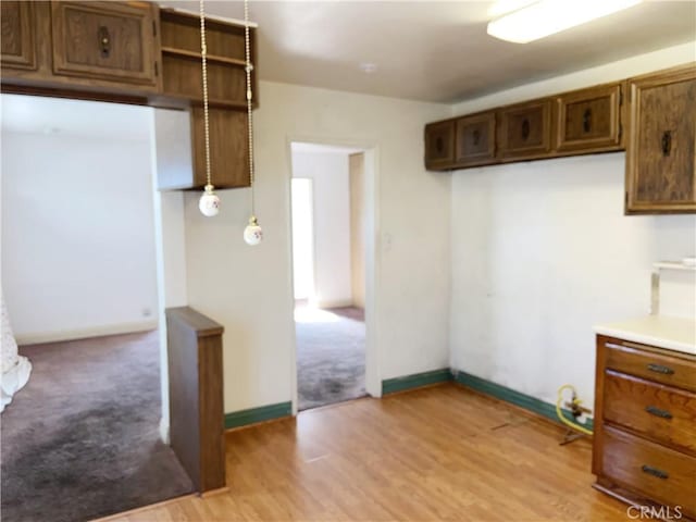 kitchen with light wood-type flooring, light countertops, decorative light fixtures, and baseboards