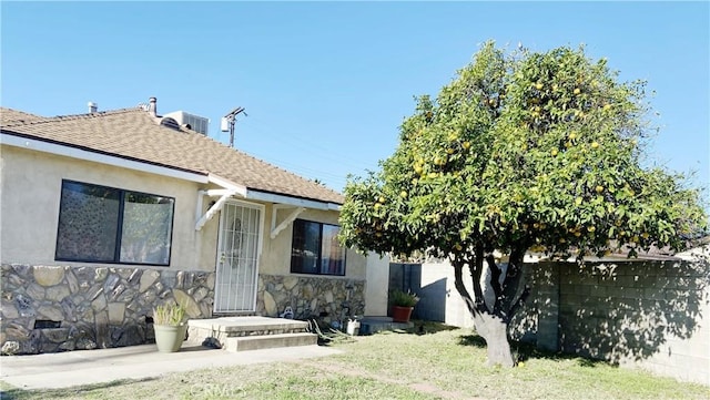 exterior space featuring stone siding, fence, stucco siding, and roof with shingles