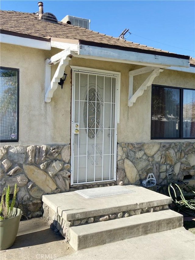 property entrance featuring a shingled roof, stone siding, and stucco siding