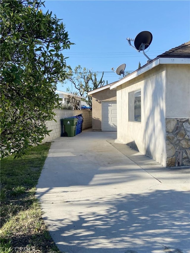 view of side of home with an outdoor structure, fence, concrete driveway, stucco siding, and a patio area