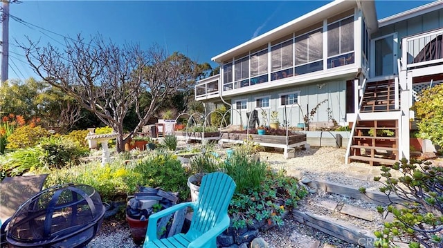 rear view of house with board and batten siding, a sunroom, a garden, and stairs