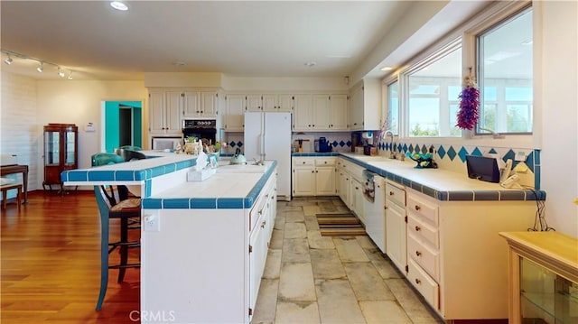 kitchen with white appliances, tile counters, white cabinets, and a sink