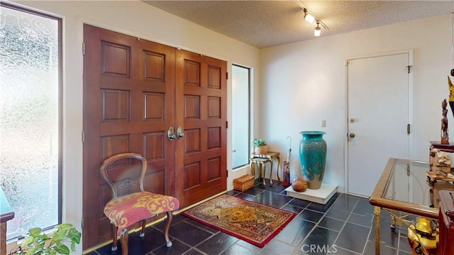 entryway with a textured ceiling, track lighting, and tile patterned floors