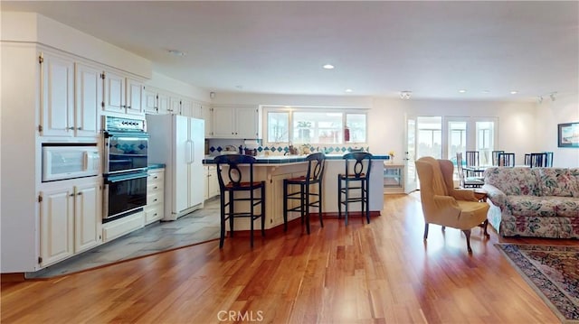 kitchen featuring tile countertops, white appliances, a kitchen breakfast bar, light wood-style floors, and white cabinets