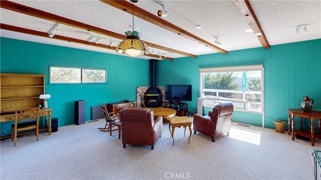 living area with a wood stove, carpet, a textured ceiling, and beamed ceiling