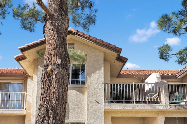 view of side of property with a tiled roof, a balcony, and stucco siding