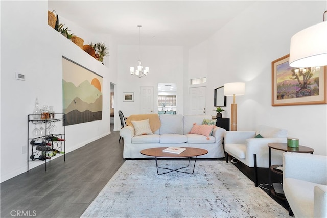 living room with a towering ceiling, baseboards, a chandelier, and dark wood finished floors