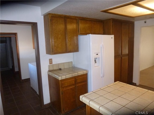 kitchen featuring white fridge with ice dispenser, dark tile patterned flooring, tile counters, and brown cabinets