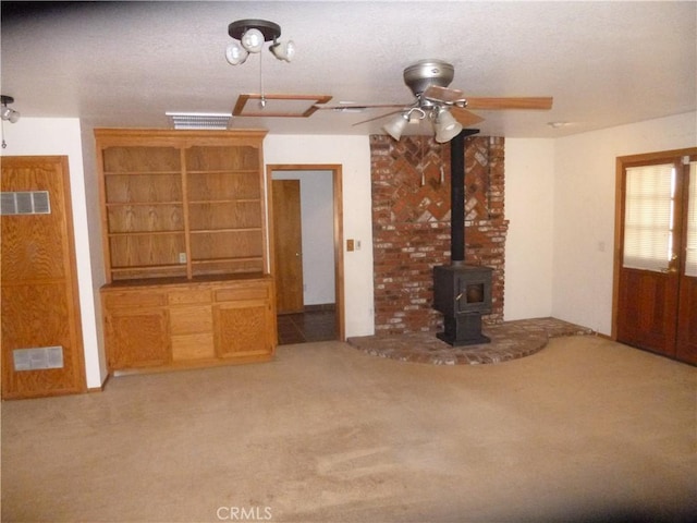 unfurnished living room featuring carpet, a wood stove, visible vents, and ceiling fan