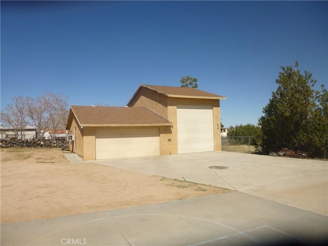 view of side of home featuring driveway, an attached garage, fence, and stucco siding