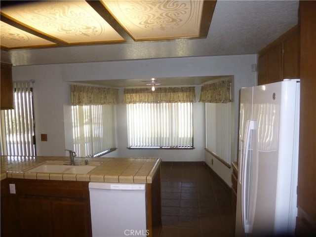 kitchen featuring tile countertops, white appliances, brown cabinets, and a sink