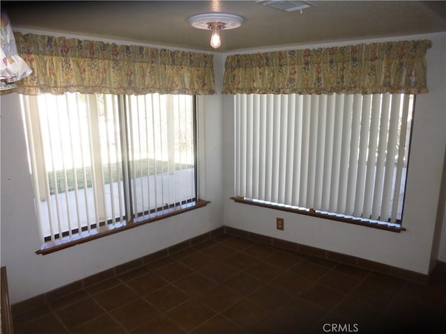 spare room featuring dark tile patterned flooring, visible vents, and baseboards