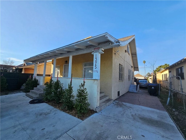 view of front of house with covered porch, fence, and stucco siding