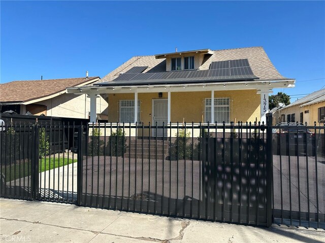 1375 E 46th St, Los Angeles, CA 90011 - exterior space featuring roof with shingles, stucco siding, roof mounted solar panels, a fenced front yard, and covered porch