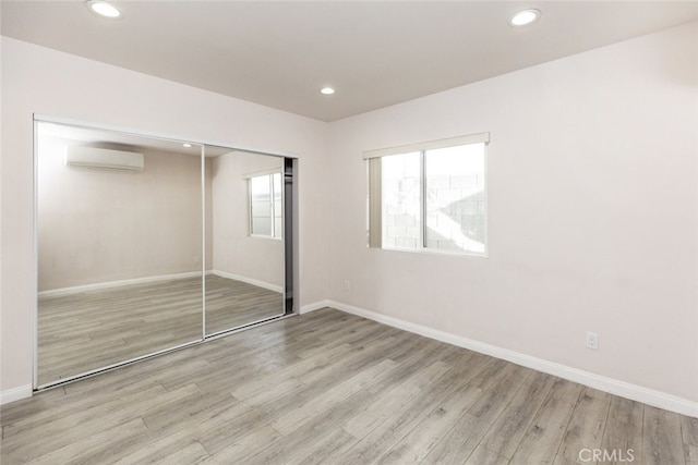 unfurnished bedroom featuring baseboards, a wall unit AC, light wood-style flooring, and recessed lighting