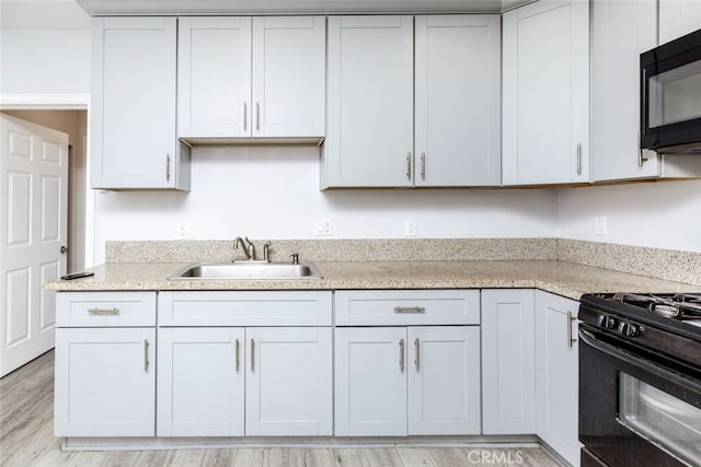 kitchen featuring black appliances, white cabinetry, light wood-style floors, and a sink