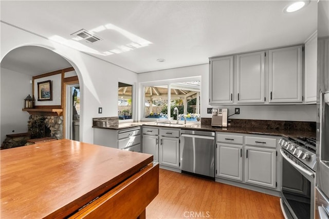 kitchen with a stone fireplace, light wood-style flooring, stainless steel appliances, a sink, and visible vents