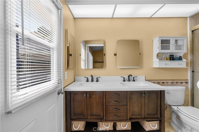 full bath with toilet, double vanity, a sink, and a shower with shower door