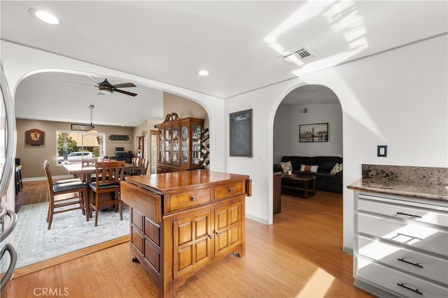 kitchen featuring light wood-style floors, visible vents, arched walkways, and a ceiling fan