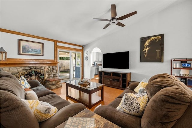 living room featuring arched walkways, lofted ceiling, ceiling fan, a stone fireplace, and wood finished floors