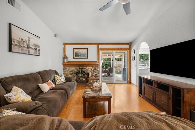 living area featuring a fireplace, visible vents, light wood-style flooring, a ceiling fan, and vaulted ceiling