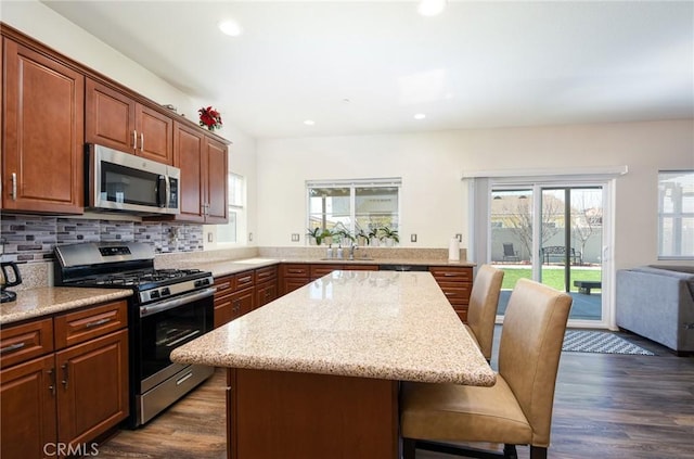 kitchen with dark wood-style flooring, appliances with stainless steel finishes, a breakfast bar area, and backsplash