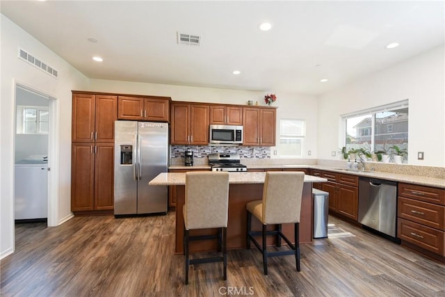 kitchen with a breakfast bar area, a kitchen island, appliances with stainless steel finishes, light stone countertops, and dark wood-style floors