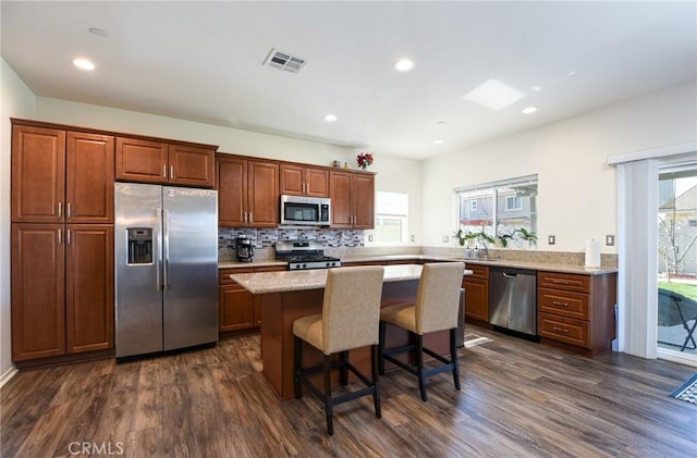 kitchen with dark wood-style flooring, stainless steel appliances, visible vents, a kitchen island, and a kitchen bar