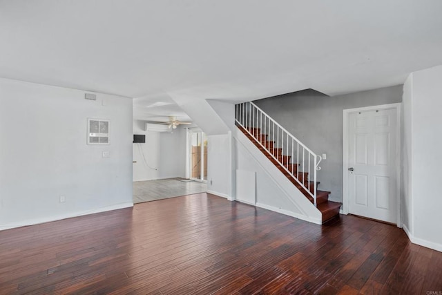 unfurnished living room featuring a ceiling fan, baseboards, an AC wall unit, stairway, and dark wood finished floors