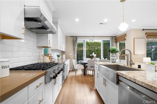 kitchen featuring decorative light fixtures, custom range hood, appliances with stainless steel finishes, white cabinets, and a sink