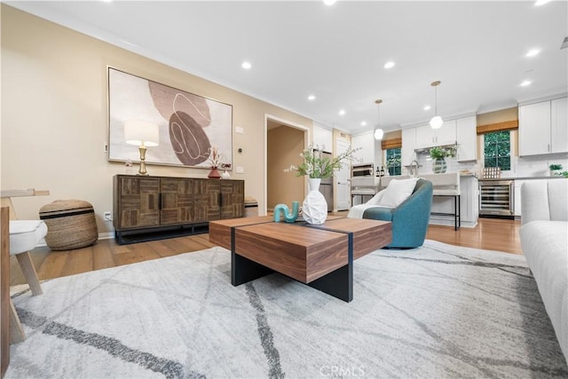 living area with light wood-style floors, beverage cooler, crown molding, and recessed lighting