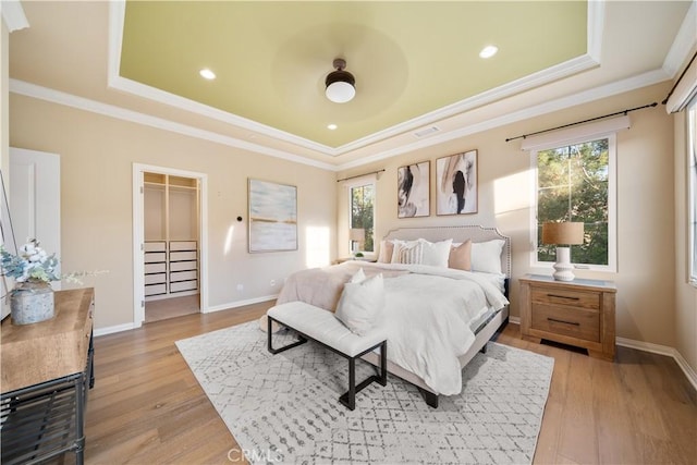 bedroom with a tray ceiling, light wood-type flooring, and baseboards