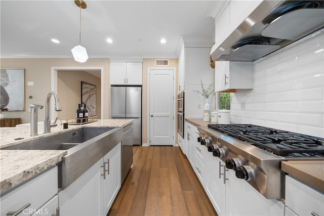 kitchen featuring pendant lighting, stainless steel appliances, white cabinets, a sink, and exhaust hood