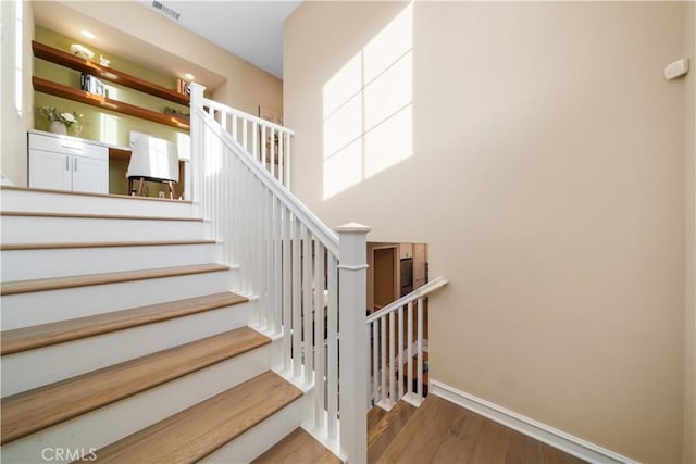 staircase with a towering ceiling, wood finished floors, visible vents, and baseboards