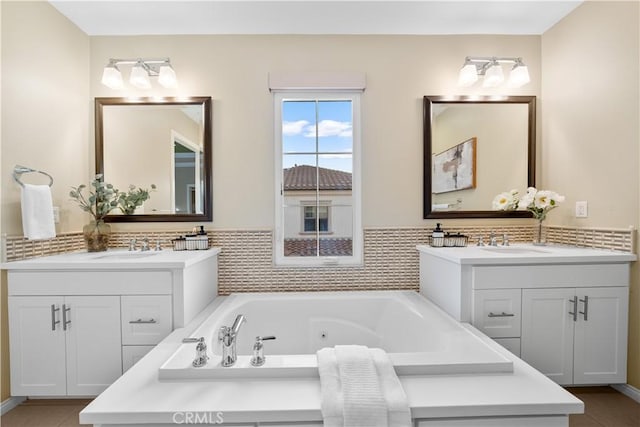 bathroom with a jetted tub, two vanities, and a sink