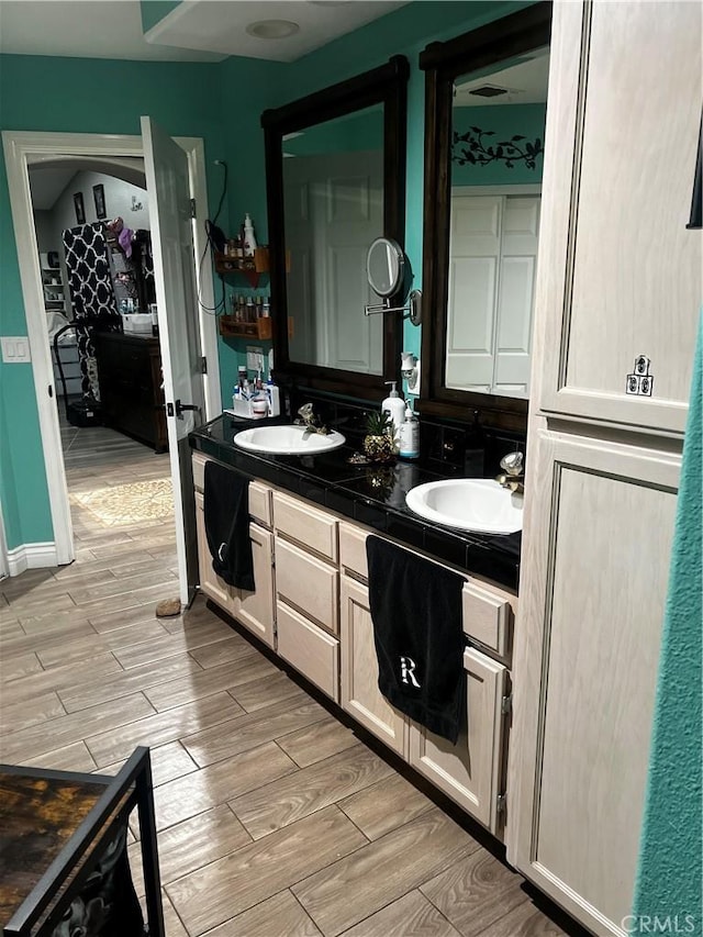 bathroom with double vanity, wood finish floors, a sink, and connected bathroom