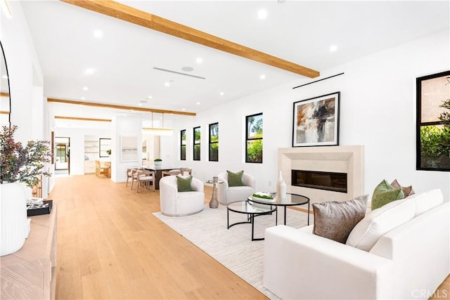 living room with light wood-style floors, recessed lighting, beamed ceiling, and a glass covered fireplace