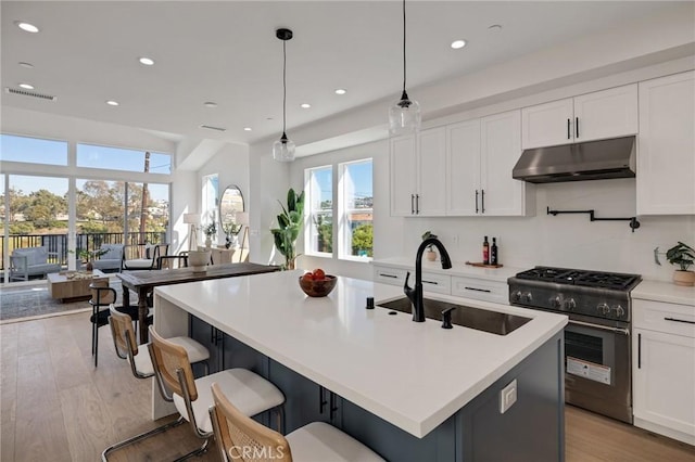 kitchen with under cabinet range hood, a sink, light countertops, high end stainless steel range oven, and decorative light fixtures