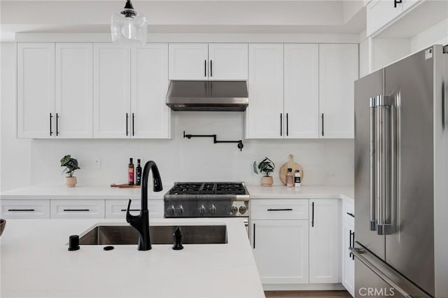 kitchen with white cabinets, premium appliances, light countertops, under cabinet range hood, and a sink