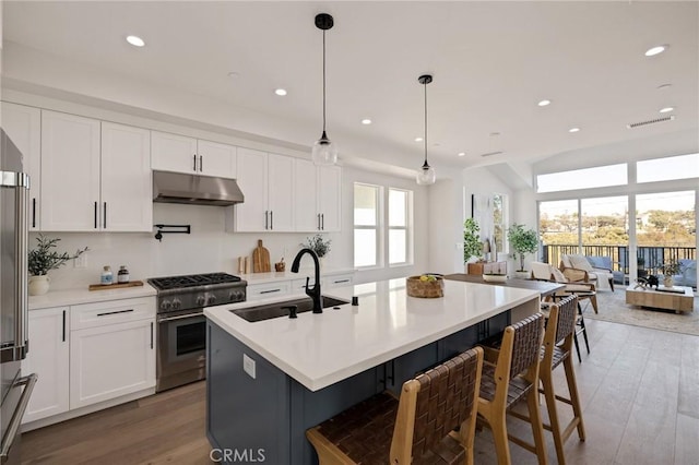 kitchen with decorative light fixtures, light countertops, high end stove, under cabinet range hood, and a sink