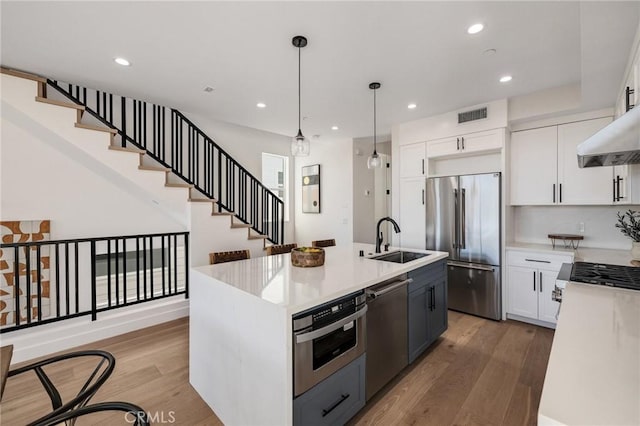 kitchen featuring a center island with sink, white cabinets, stainless steel appliances, light countertops, and a sink