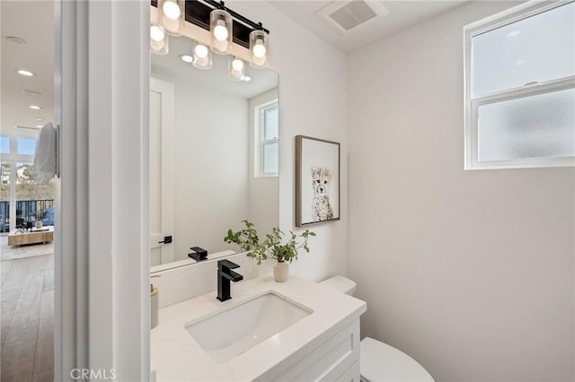 half bathroom featuring visible vents, wood finished floors, vanity, and toilet