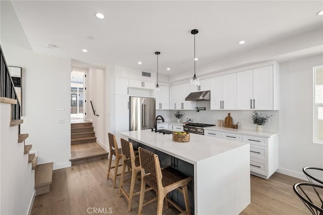 kitchen with a center island with sink, high end fridge, light countertops, white cabinets, and under cabinet range hood