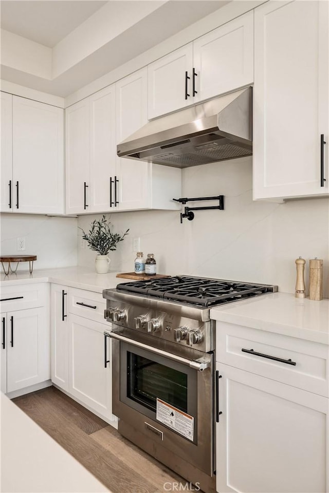 kitchen featuring stainless steel stove, light countertops, white cabinetry, wood finished floors, and under cabinet range hood