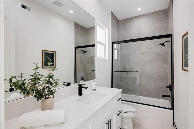 full bath featuring visible vents, vanity, toilet, and bath / shower combo with glass door