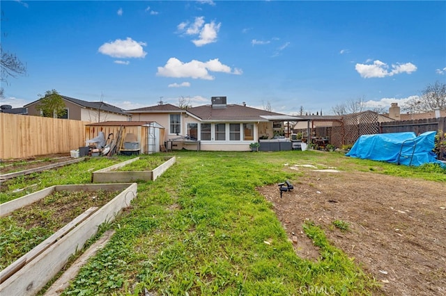 rear view of house with a garden, a lawn, and a fenced backyard