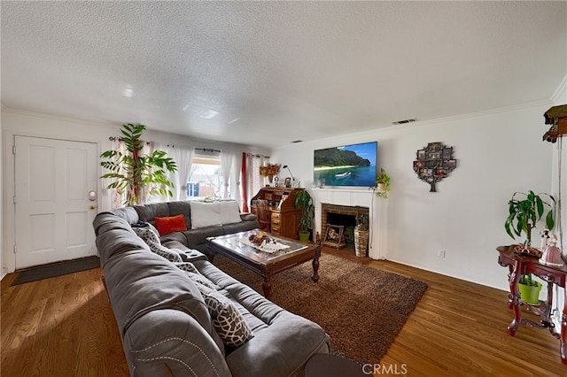 living room featuring a fireplace with flush hearth, visible vents, a textured ceiling, and wood finished floors